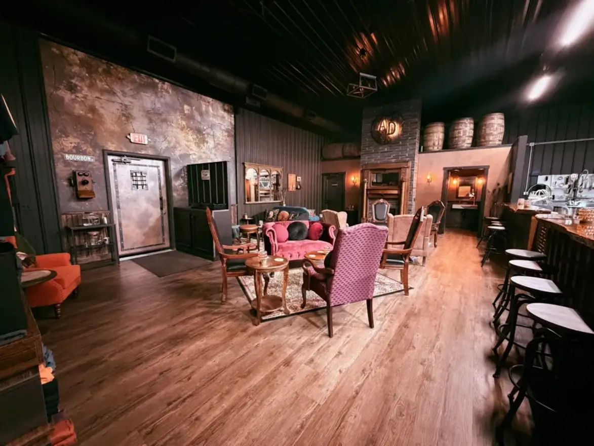 The full speakeasy parlor: velvet chairs and fireplace on one side, the bar and stools on the other