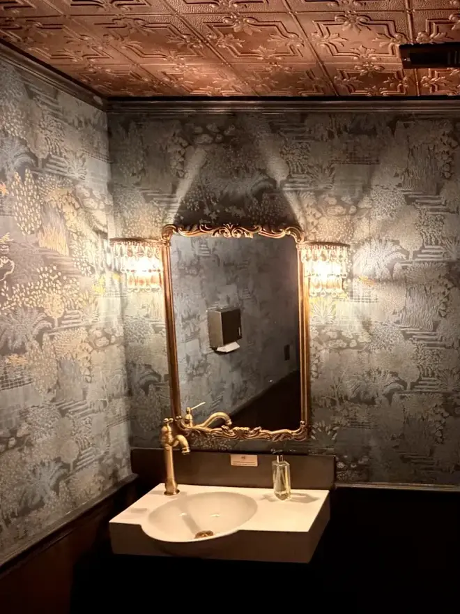 The powder room, with a pressed-tin ceiling, gilt mirror, and brass fixtures