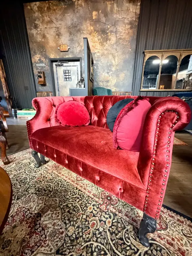 A red velvet tufted settee on a Persian rug in the speakeasy lounge
