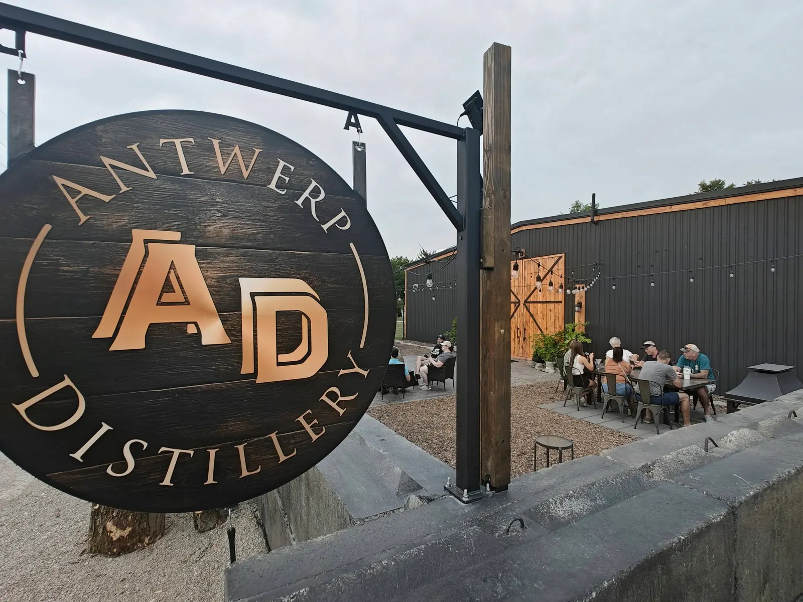 The hanging Antwerp Distillery sign with the outdoor patio and string lights beyond